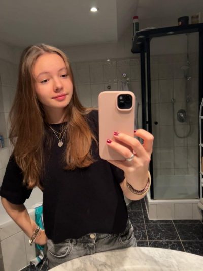 Eine junge Frau in einem Badezimmer mit einem Smartphone in der Hand, sie nimmt ein Selfie auf.